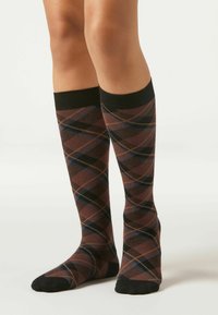 Bruine kniehoge sokken met een geruit patroon in zwart, blauw en beige, met een effen zwarte boord aan de bovenkant en een textuurstof.