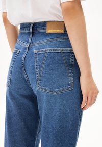 Hoge taille blauwe denim jeans met een bruine gestikte label, twee achterzakken met gestructureerde naden en een klassieke vervaagde textuur.
