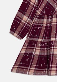 Vinröd rutig klänning av mjukt tyg med ljusrosa och grå rutor, långa ärmar och utspridda silverstjärnor.