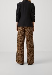 Černé přizpůsobené sako v kombinaci se širokými kalhotami s leopardím potiskem v odstínech hnědé a černé, s hladkou texturou a pohodlným střihem.