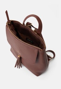 Bolsa de mão em couro castanho com fecho na parte superior, bolso frontal e ferragens douradas. Apresenta um detalhe de franjas e um interior forrado.