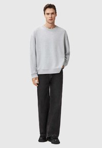 Szary bawełnowy sweatshirt z okrągłym dekoltem, luźny krój i ścięte mankiety, w połączeniu z szerokimi czarnymi dżinsami i czarnymi butami. Minimalistyczny design.