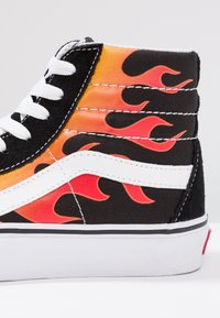 Høj-top sneakers med en sort kanvasbase, prydet med orange og røde flammegrafikker, hvide detaljer og sorte snørebånd. Hvid gummisål.