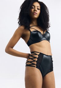 Svart undertøy sett som inkluderer en formet bh med stroppdetaljer og høyhårede truser med mesh-paneler og snøring.
