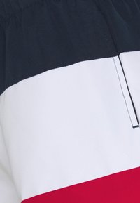 Shorts colorés en blocs dans des teintes marine, blanche et rouge. Fabriqués en tissu léger avec une taille élastique et une poche arrière. Détails des coutures à plat.