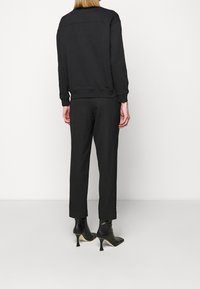 Felpa nera con vestibilità rilassata, polsini e orlo a coste, abbinata a pantaloni neri affusolati coordinati e stivaletti neri con punta appuntita.