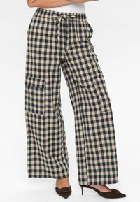 Pantalons à jambes larges, à carreaux beiges et navy avec une taille élastique, cordon de serrage et poches latérales. Le tissu a une apparence douce et texturée.