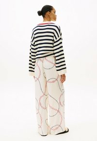 Maglione a righe di maglia in navy e crema, con un colletto rosso, abbinato a pantaloni larghi color crema con un motivo a catena in rosa e nero.