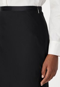 Fustă neagră tip creion cu o textură netedă, închidere cu fermoar detaliată și un tiv din satin cu un logo subtil Calvin Klein.