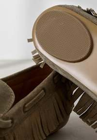 Zapato mocasín de ante marrón con detalles de flecos, puntera redondeada y suela de goma texturizada con estrías horizontales.