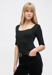 Mustassa, ribbineulospuserossa on neliskanttinen pääntie ja pitsireunus, lyhyet hihat. Yhdistetty korkeavyötäröisiin mustiin housuihin ja vyöhön.