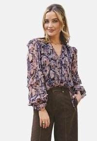 Langærmet bluse med et pink og lilla slangeprint, med flæser, dyb V-hals og afslappet pasform. Sammen med mørkebrun bukser.