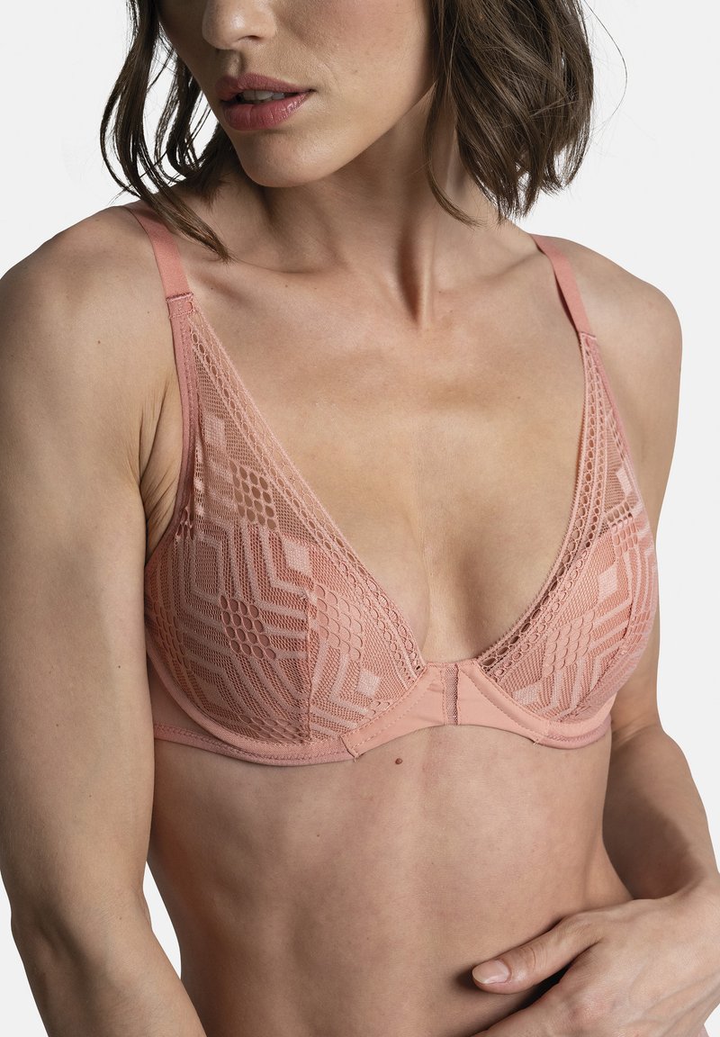 Bralette triangle en pêche clair avec une superposition de dentelle présentant des motifs géométriques. Bretelles réglables et fermeture à crochet à l'arrière. Texture douce.