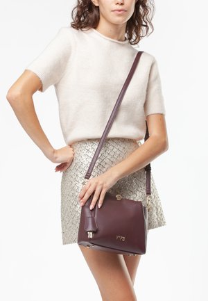 Borsa a tracolla in pelle bordeaux con hardware dorato, caratterizzata da una forma strutturata, tasca laterale e logo impresso. Texture liscia, tracolla regolabile.