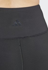 Mustad kõrge taljelega mustad retuusid, valmistatud venivast materjalist, millel on matt must Adidas'i logo ja lapikud õmblused sujuva viimistluse jaoks.