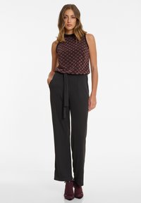 Zwarte jumpsuit met een patroon op de mouwloze top, voorzien van een tailleband en wijde benen. Aangevuld met hoge hakken en contrasterende sokken tot de enkel.