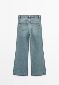 Lichtblauwe spijkerbroek met wijde pijpen, achterzakken, riemlussen en zichtbare stiknaden aan de achterkant, plat gelegd vanuit de achterkant.