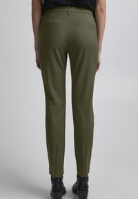 Olivengroene, op maat gemaakte broek met een slim fit, met achterzakken en een nette tailleband, gecombineerd met zwarte enkellaarzen.