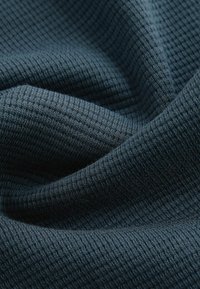 Tamsiai mėlynas tekstūruotas audinys su tinklo raštu, pasižymintis minkštu, raukšlėtu paviršiumi. Medžiaga atrodo šilta ir šiek tiek pūkuota.