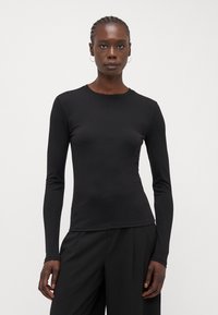 Black long-sleeve shirt with a round neckline, fitted shape, smooth texture, and minimal seam detailing, paired with black trousers.