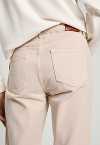 Beige džíny z denimu s rovnými nohavicemi, zadními kapsami s jemně zakřiveným stehem a s koženým štítkem značky na pásku.