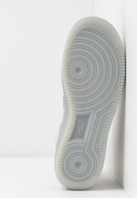 Nike-kenkäpohja, läpinäkyvää kumia, jossa on urakuvioita. Vaaleanharmaa, jossa on pyöreitä ja aaltojakoisia tekstuureja. Sivussa logo.