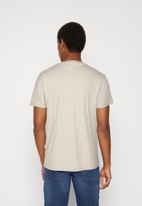Tricou din bumbac bej deschis, cu guler rotund și mâneci scurte. Design cu croi drept, cusături minime și o etichetă mică a brandului la tiv.