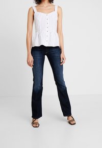 Biała bluzka peplum w paski, z kwadratowym dekoltem i guzikami, w połączeniu z ciemnoniebieskimi dżinsami z szerokimi nogawkami oraz czarnymi sandałami na paski.