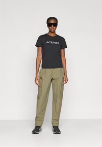 Μαύρο βαμβακερό t-shirt με λογότυπο "TERREX", συνδυασμένο με χακί παντελόνι cargo με τσέπες. Μαύρα γυαλιά ηλίου και σκούρα παπούτσια ολοκληρώνουν την εμφάνιση.