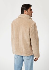 Giacca in pelliccia sintetica beige con ampio colletto, vestibilità comoda, tasche laterali e design senza cuciture. Tessuto morbido e dettagli minimi.