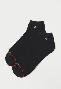 Calcetines tobilleros negros con detalles rojos, tela suave, punta redondeada y detalle del logo en blanco en cada calcetín. Textura suave, sin patrones.