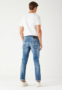 Vaqueros de mezclilla azules con corte ajustado, que presentan una textura ligeramente desgastada, puños enrollados y una etiqueta en la parte trasera de la cintura.