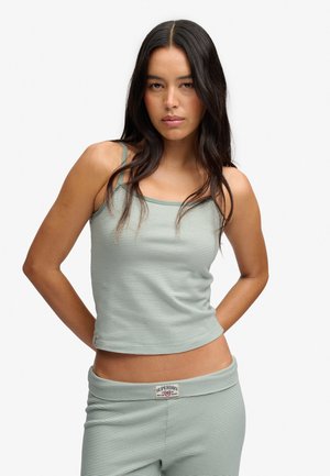 Femme aux longs cheveux foncés portant un débardeur rayé vert clair et blanc et un pantalon assorti avec une étiquette Superdry.