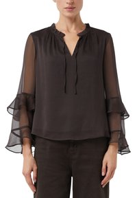 Blouse noire transparente avec col en V à volants et manches longues ornées de volants superposés. Tissu léger, coupe décontractée et détails minimalistes.