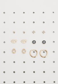 Roza zlato uhani prikazujejo različne oblike: dve pari uhane na razpotju, oblike oči, ročne motive, cvetlične oblike in okrogle naglavne kamenčke na perforirani podlagi.