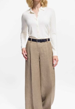 Camicia bianca a maniche lunghe con bottoni, abbinata a pantaloni larghi di lino marrone chiaro. L'outfit è completato da una cintura intrecciata scura con fibbia in argento.