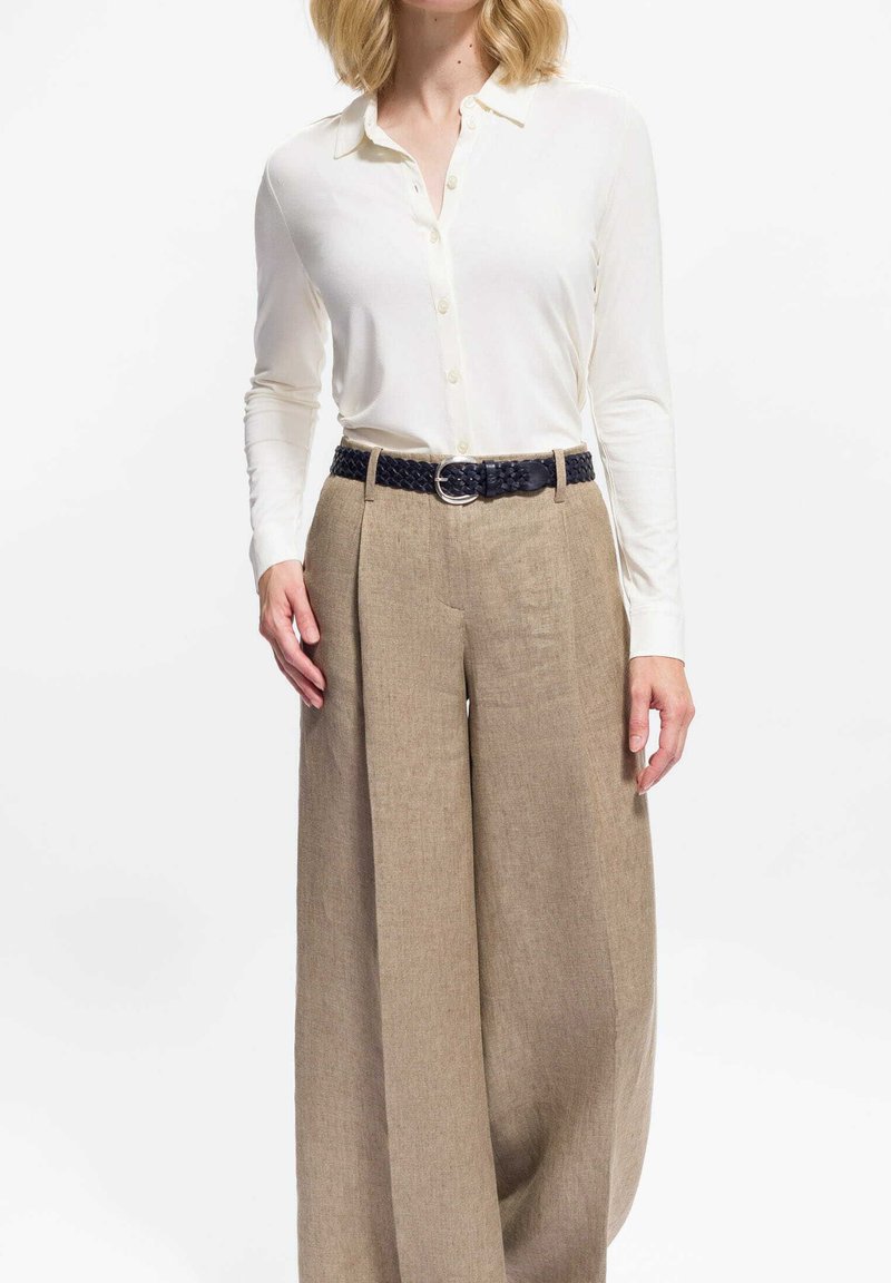 Biała koszula z długim rękawem i guzikami, zestawiona z luźnymi, jasnobrązowymi lnianymi spodniami. Stylizacja uzupełniona ciemnym plecionym paskiem z srebrną klamrą.