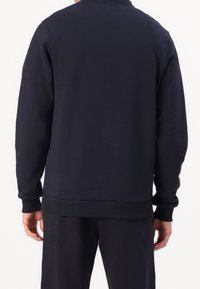 Sudadera azul marino hecha de algodón suave, con un corte relajado, puños y dobladillo acanalados. Textura lisa sin patrones ni logotipos visibles.