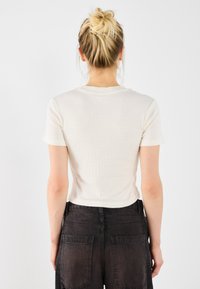 Korte mouwen ribbel top in crème met een ronde halslijn; gecombineerd met high-waisted donkergrijze broeken met grote achterzakken.