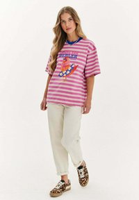 Růžové a bílé pruhované tričko s grafickým designem ptáka na talíři, spárované s krémovými kalhotami a teniskami s leopardím vzorem.