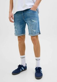 Lichtblauwe denim shorts met opgerolde manchetten, voorzien van versleten patches en een klassieke vijf-pocket ontwerp. Draag ze met marineblauwe sneakers en witte sokken.