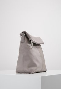 Šedá semišová kabelka přes rameno s přeloženým vrškem, stříbrným kováním, boční zipovou kapsou a měkkou, hladkou texturou. Design se vyznačuje minimalistickým tvarem.