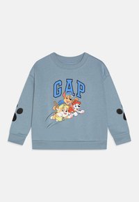 Lyseblå hettegenser med grafikk av tegneseriehunder og "GAP" i fet blå skrift, med svarte prikker på ermene.