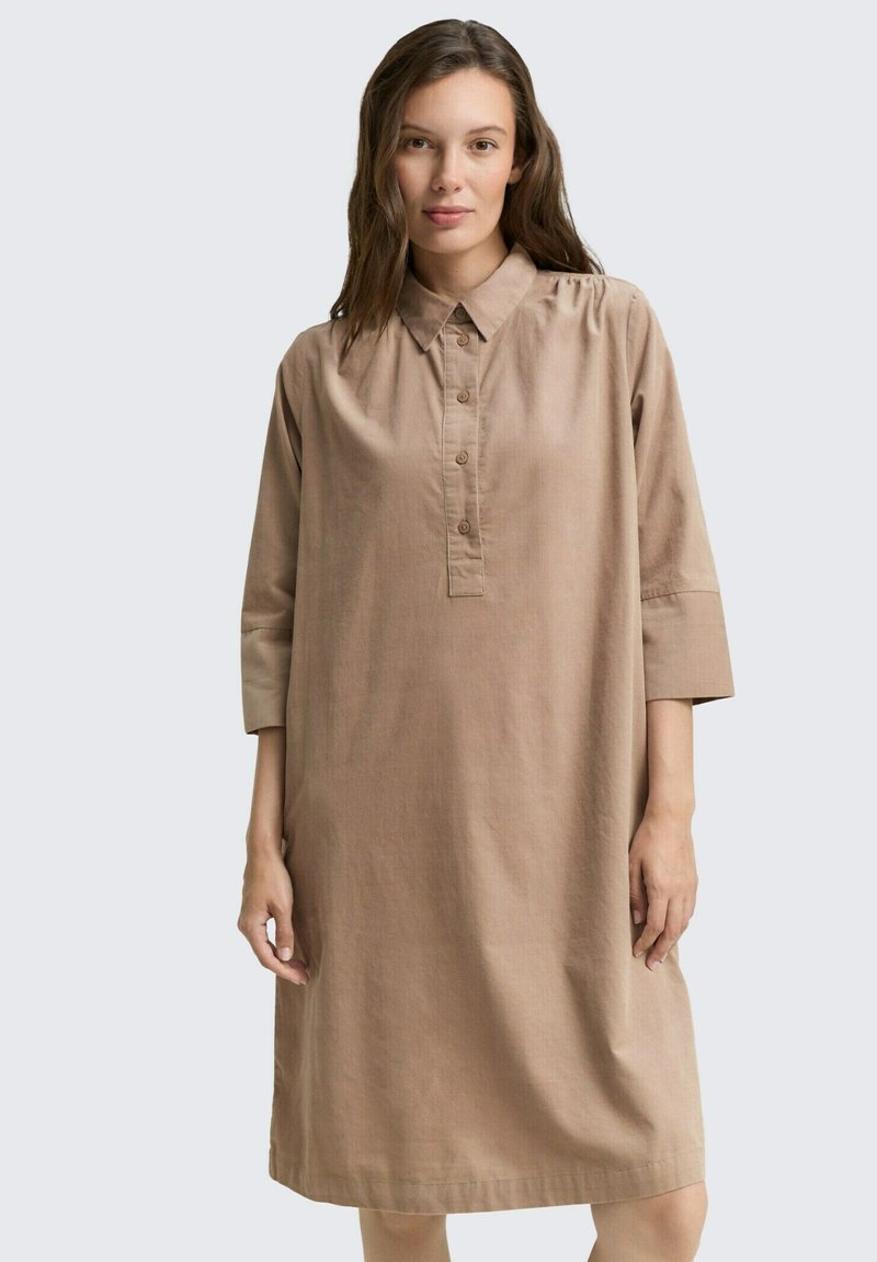 Locker sitendes, langärmliges Kleid aus hellbraunem Stoff. Verfügt über eine Knopfleiste und einen Kragen. Midikleid-Länge. Glatte Textur.