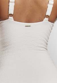 Tissu blanc texturé avec un délicat motif froissé. Doté de bretelles réglables avec des éléments en métal doré et d'un petit accent en métal portant la marque.