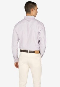 Paarse en witte gestreepte lange mouwen shirt op een model, gecombineerd met crèmekleurige broek en een bruine riem met leren accent.