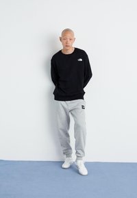 Sort sweatshirt med rund hals og lille logo, parret med lysegrå sweatpants med et sort logo-patch. Hvide sneakers fuldender outfittet.