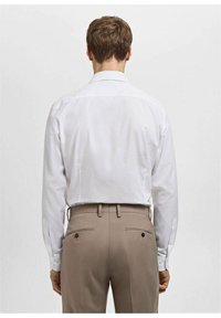 Biała koszula z długim rękawem z klasycznym kołnierzykiem, gładko dopasowany tył, w połączeniu z beżowymi spodniami z guzikami na kieszeniach.