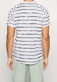 Randig t-shirt i vitt, svart och grått, med horisontella linjer av varierande bredd och en böjd nederdel. Korta ärmar, lättviktigt tyg.