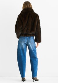 Brown faux fur jacket with high collar, worn over a light blue, relaxed-fit denim jeans. The jacket features a soft texture and a cropped silhouette.